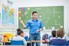 Photo of a teacher and their young students  together in a classroom. Ideally, the teacher  is speaking or writing something on the board.