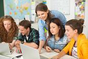 Photo of students in a classroom discussing something with their teacher, or working together as a group.