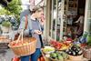 Young woman standing on street outside food shop looking at fresh produce on stall.