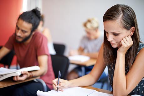 134098 Three college students sitting an exam in a classroom writing.